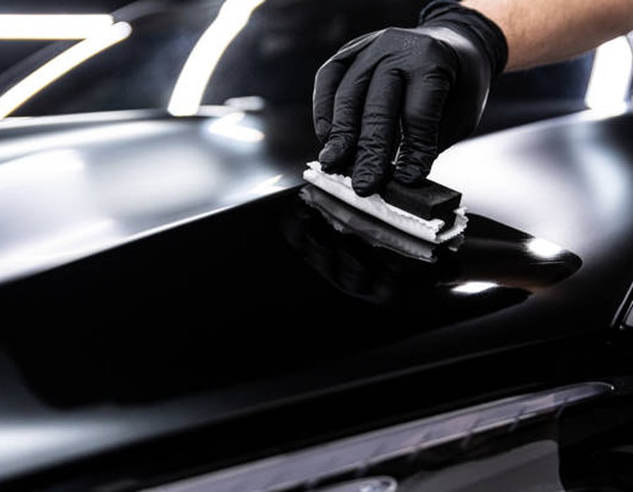 Technician hand-applying ceramic coating to a vehicle hood