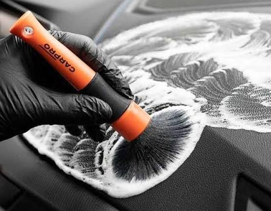 Detail brush cleaning a vehicle dashboard with foam cleaner